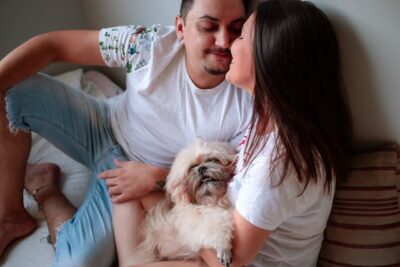 A Couple Kissing Each Other while Holding a Shih Tzu pup